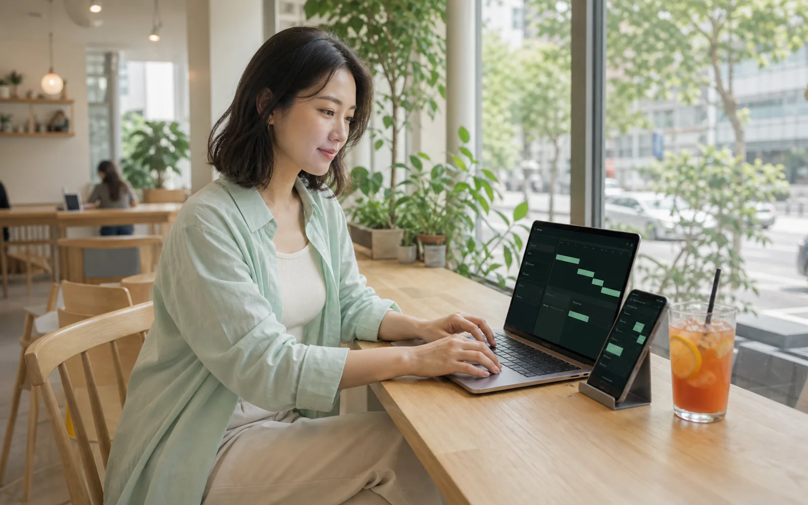 Adult woman reviewing a project timeline on a laptop and phone in a bright café